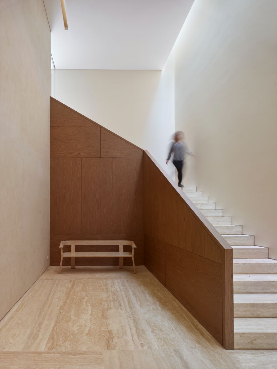 The L-shaped stairs are constructed with light wood steps all the way to the flooring and dark wood handrails. The space is illuminated by the skylight.