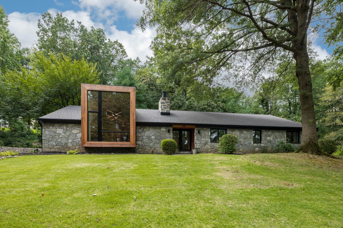 A stone-walled home exterior is a perfect complement to the cedar-clad modern dormer. Facing a large lawn surrounded by mature trees.