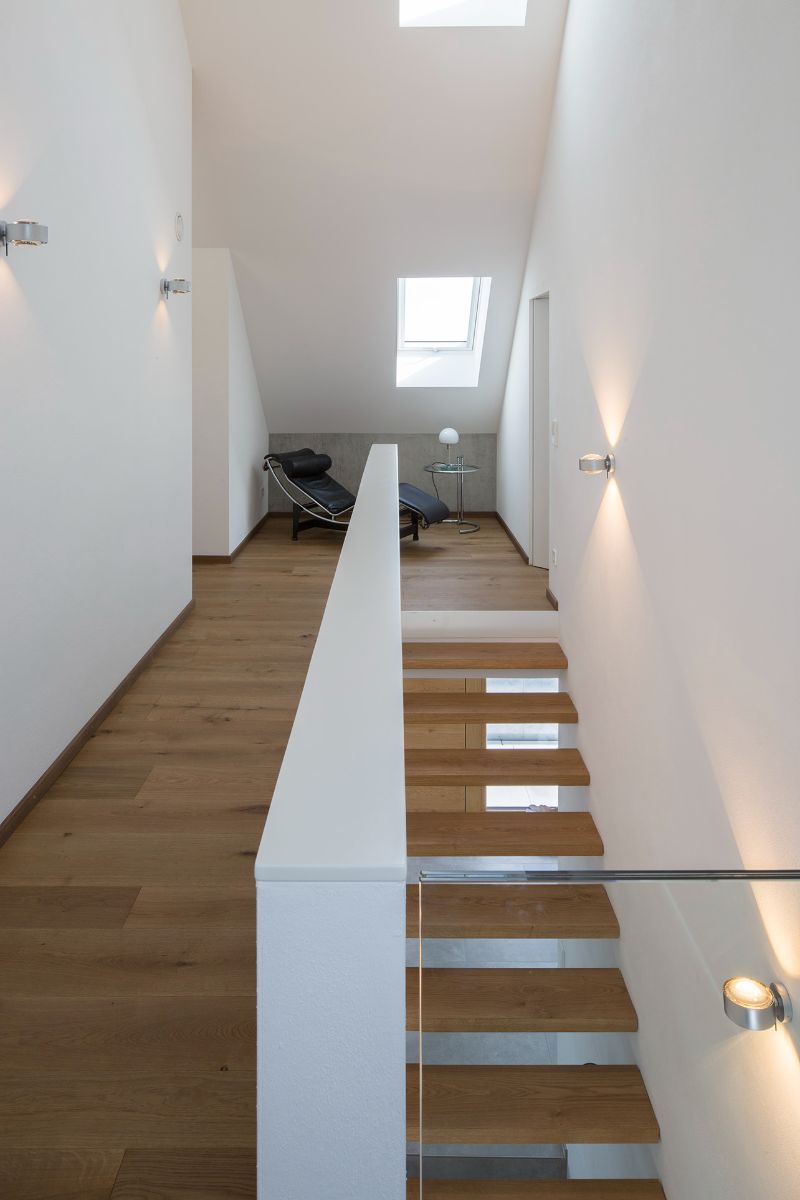 An simple wooden stairway lighted by skylights leads to the attic, which contains individual rooms. 
