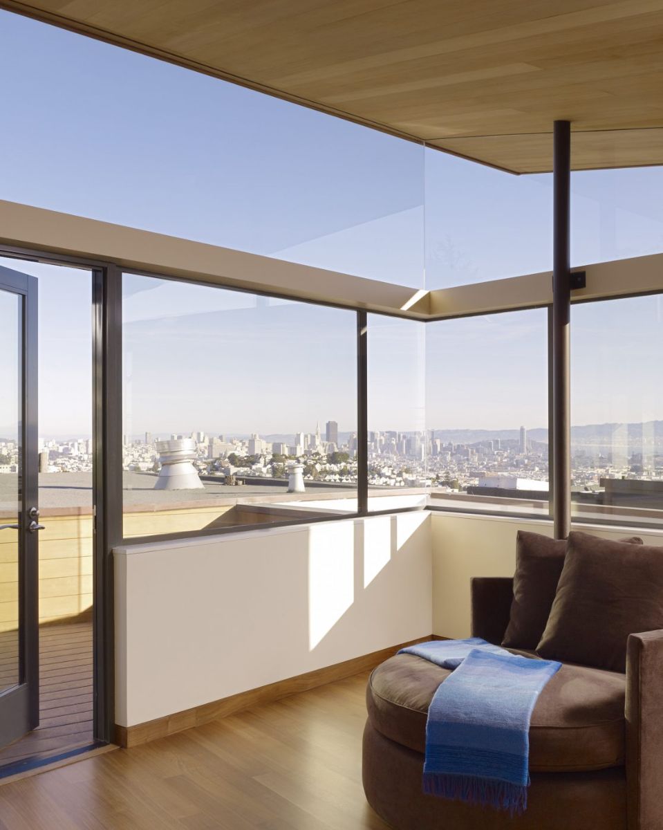 A light-filled and spacious open living room surrounded by glass, with a door leading to a terrace with a panoramic view of the city.