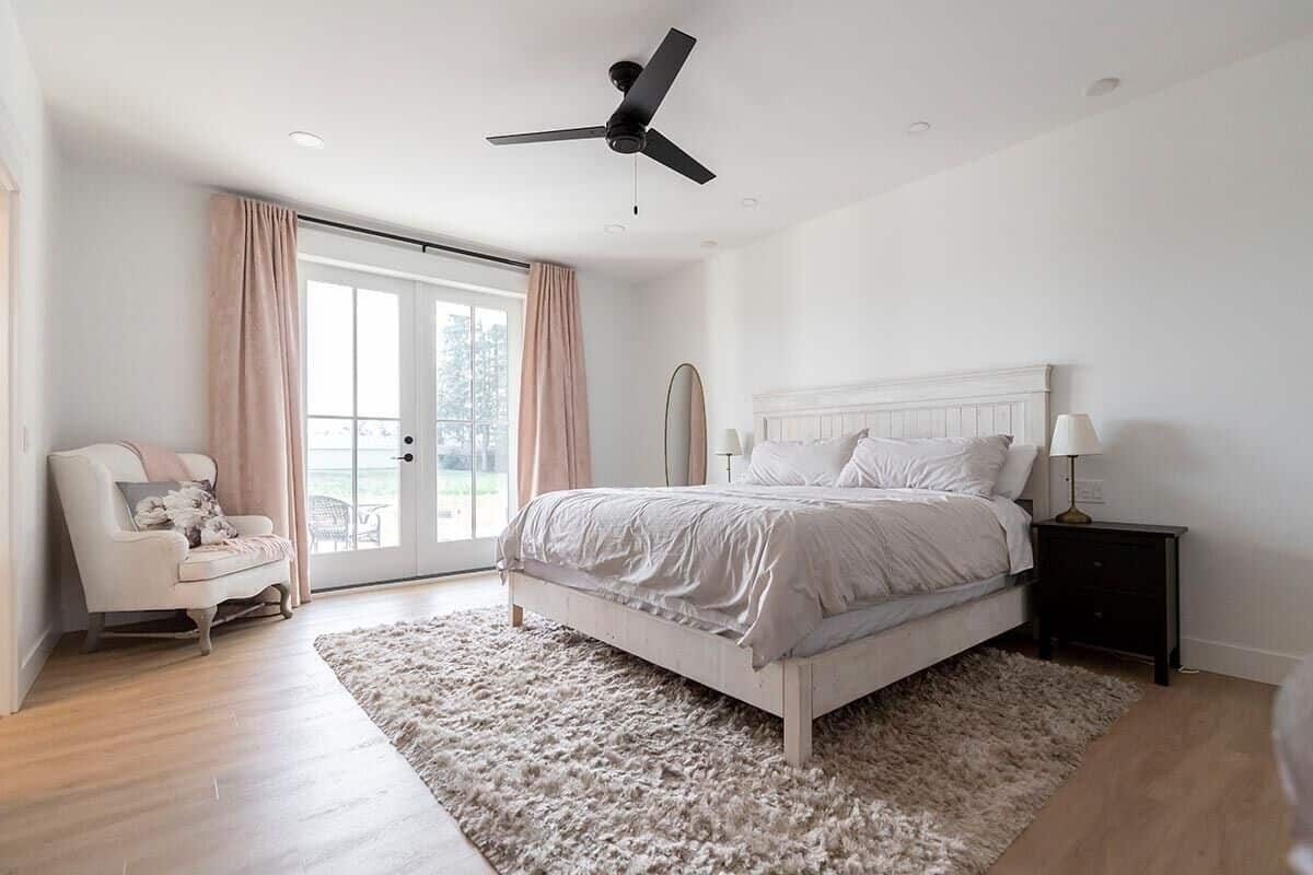 The primary bedroom has a distressed white bed, a wingback armchair, and direct outdoor access via a French door.