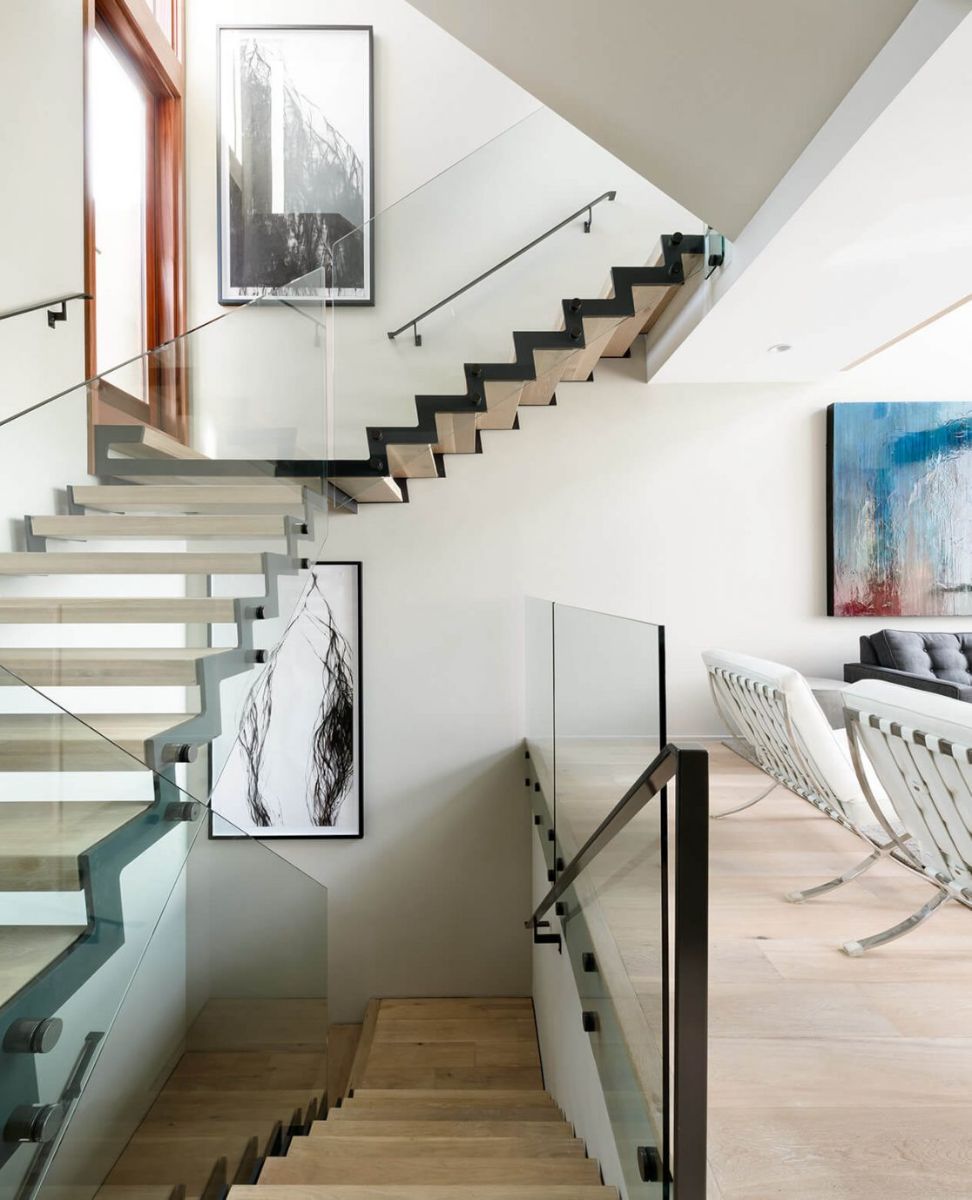 An inventively designed floating staircase with hardwood steps and a glass railing. The artworks decorate the area.