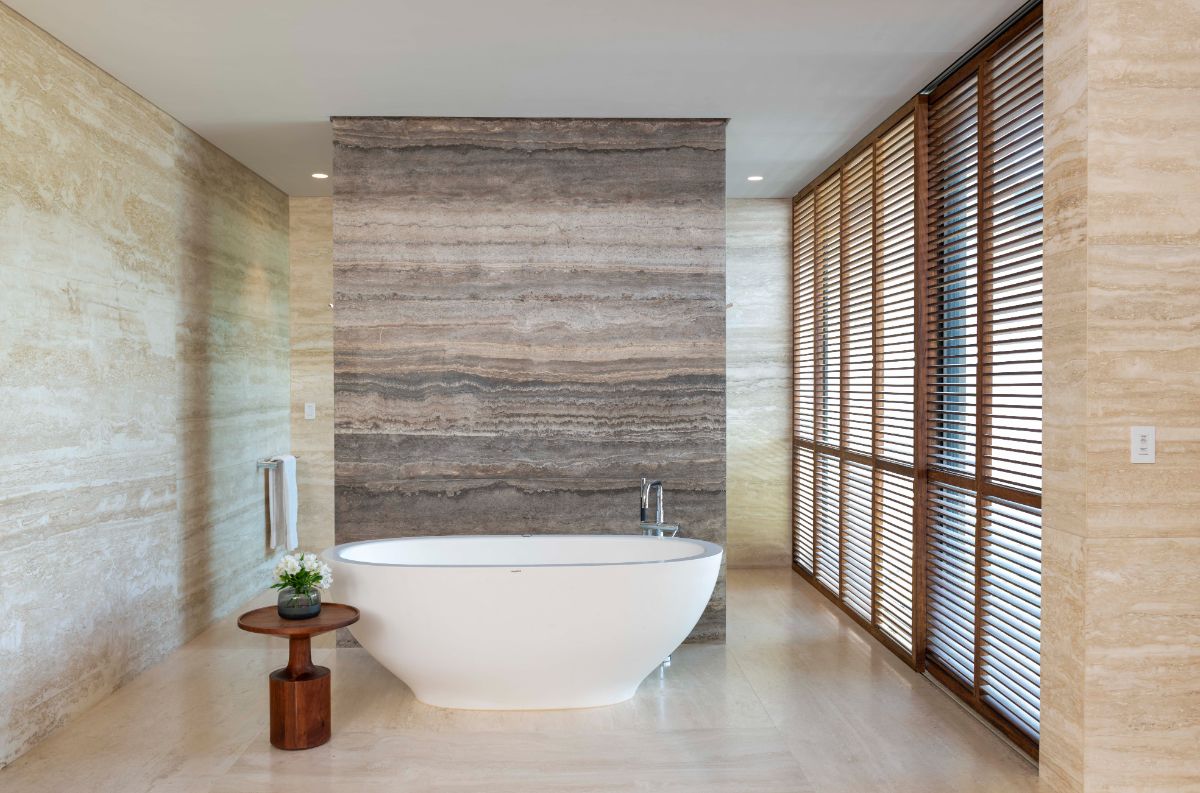 A modern bathroom with a freestanding tub, lightwood flooring, and a stone wall. The bathroom is designed to provide extra privacy.
