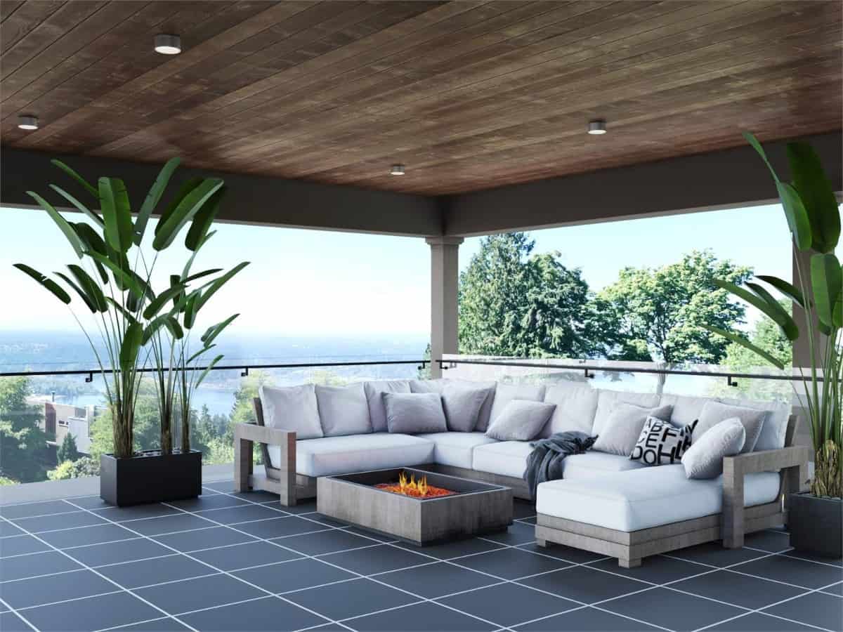 The covered deck has a fire pit table and glass railings overlooking the surrounding landscape.