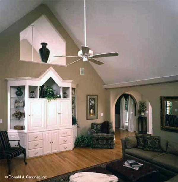 The great room has classic seats, a white cabinet, and a cathedral ceiling mounted with an industrial fan.