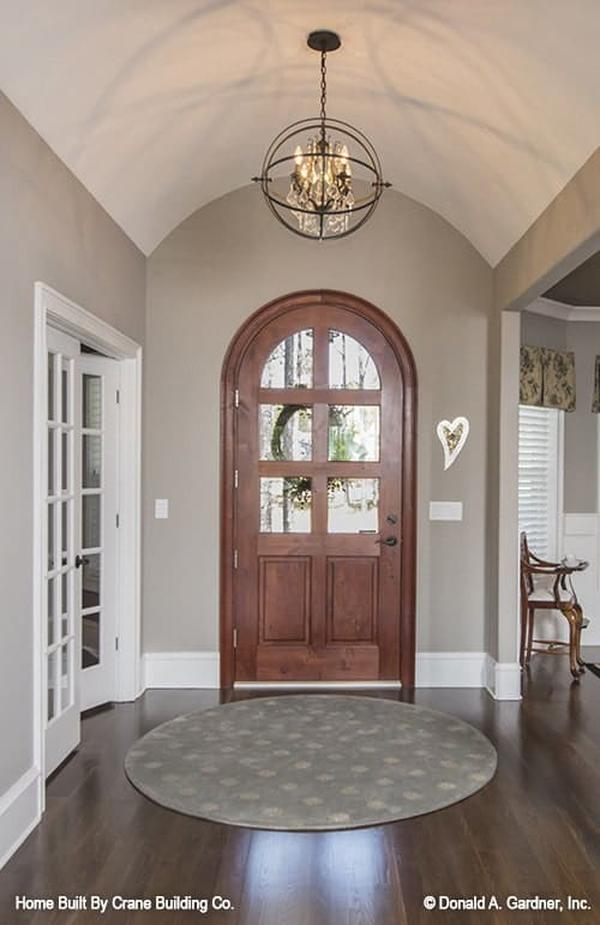 The arched entry door reveals the foyer with a spherical chandelier and a round area rug.