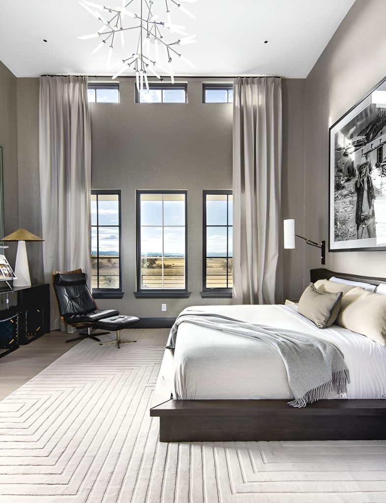 Primary bedroom with a platform bed, leather lounge chair, and a tall ceiling complemented with a statement chandelier.