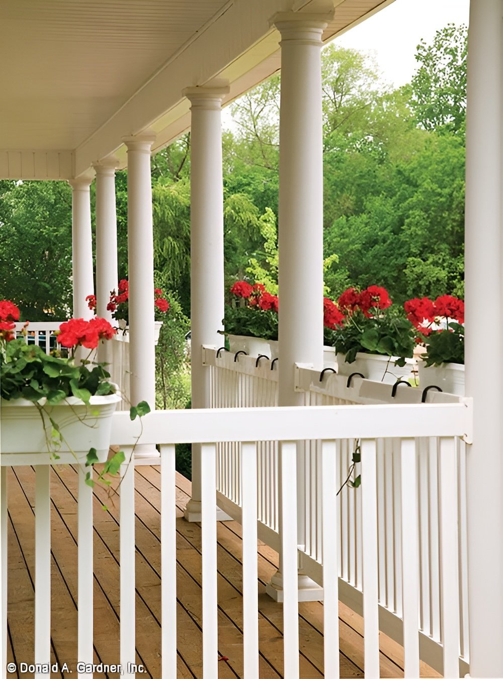 Covered front porch with wide plank flooring, white railings, and round columns.