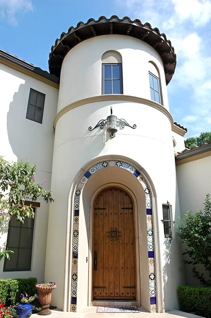 An arched home entry fitted on the large turret. It features a wooden front door framed with decorative tiles.