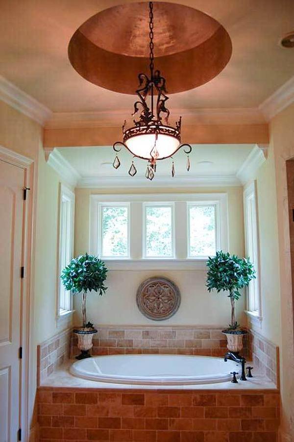 The deep soaking tub clad in tiled bricks is illuminated by a wrought iron chandelier hanging from the round tray ceiling.
