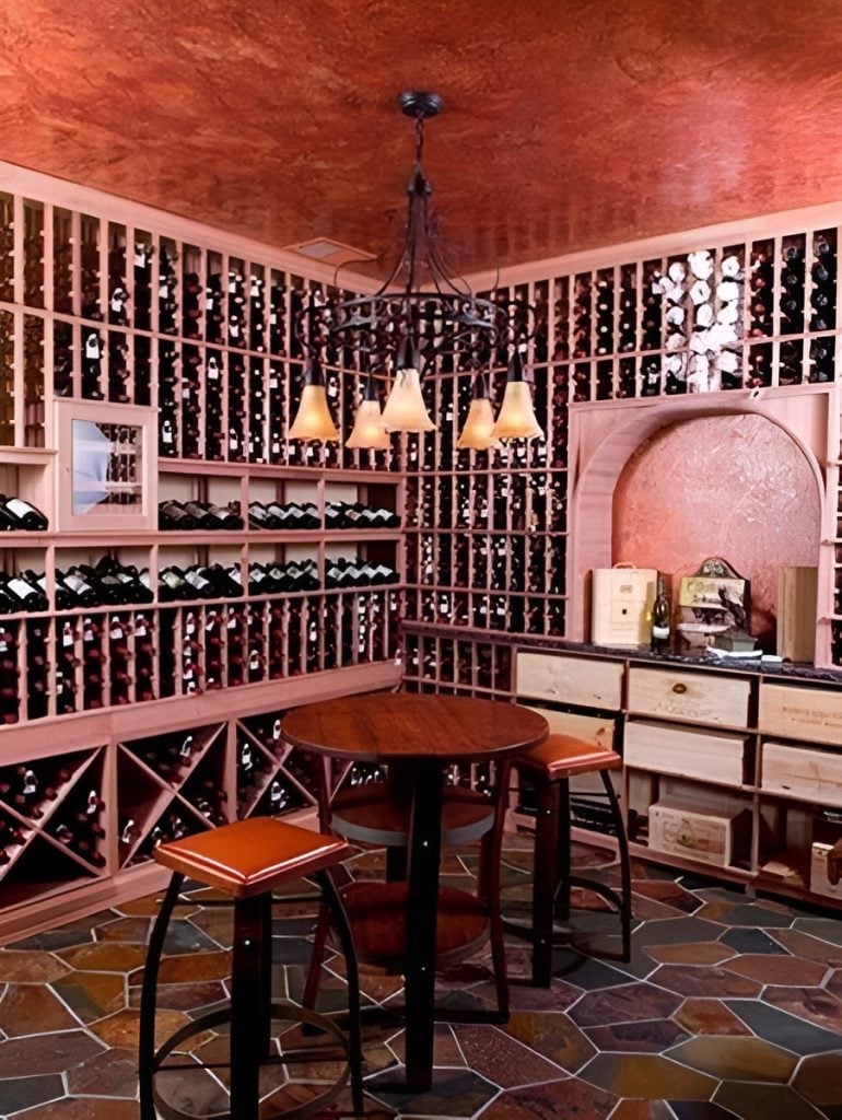 The wine cellar is filled with column shelves centering around the wooden stools and a round table lit by a wrought iron chandelier.