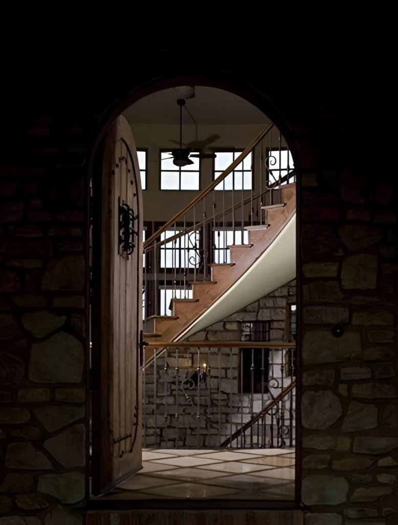 An arched wooden door opens to the main floor balcony with stone walls and plenty of small windows that bring natural light in.