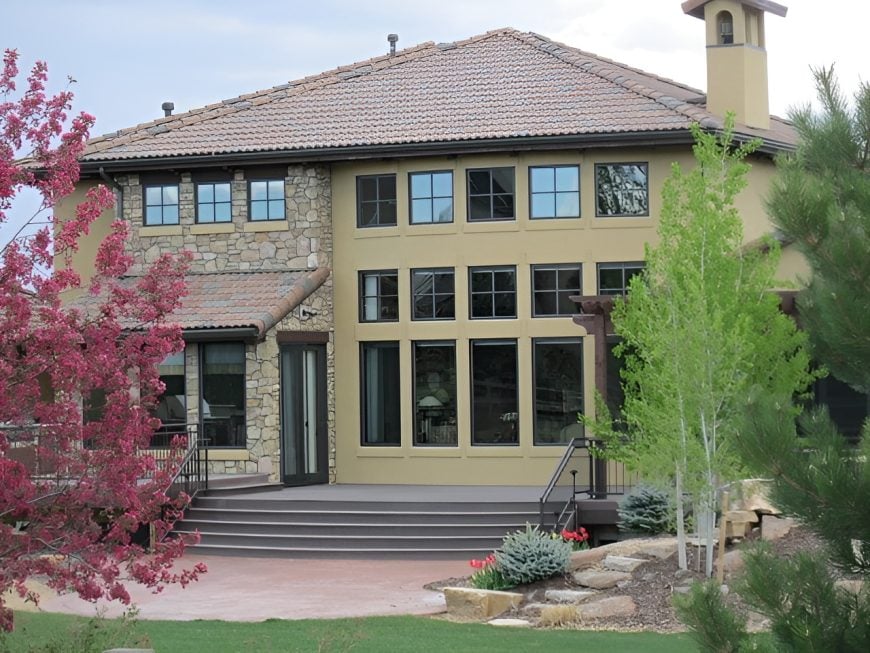 Home's rear view showing the patio and a serene garden filled with gorgeous plants and a lush lawn.