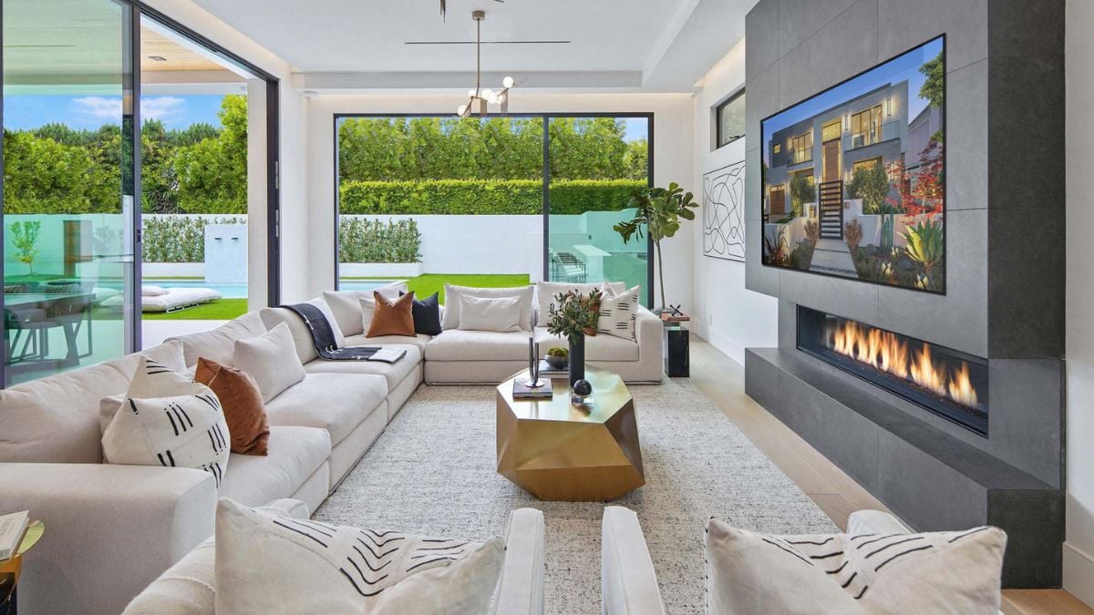 The Great Room showcases a sleek, floor-to-ceiling fireplace with a captivating black tile finish, complemented by three sets of full-height sliding glass doors revealing the pool.