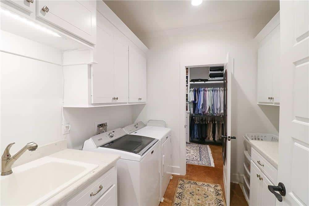 The primary walk-in closet connects with the laundry room equipped with lots of storage, top-load appliances, and a sink.