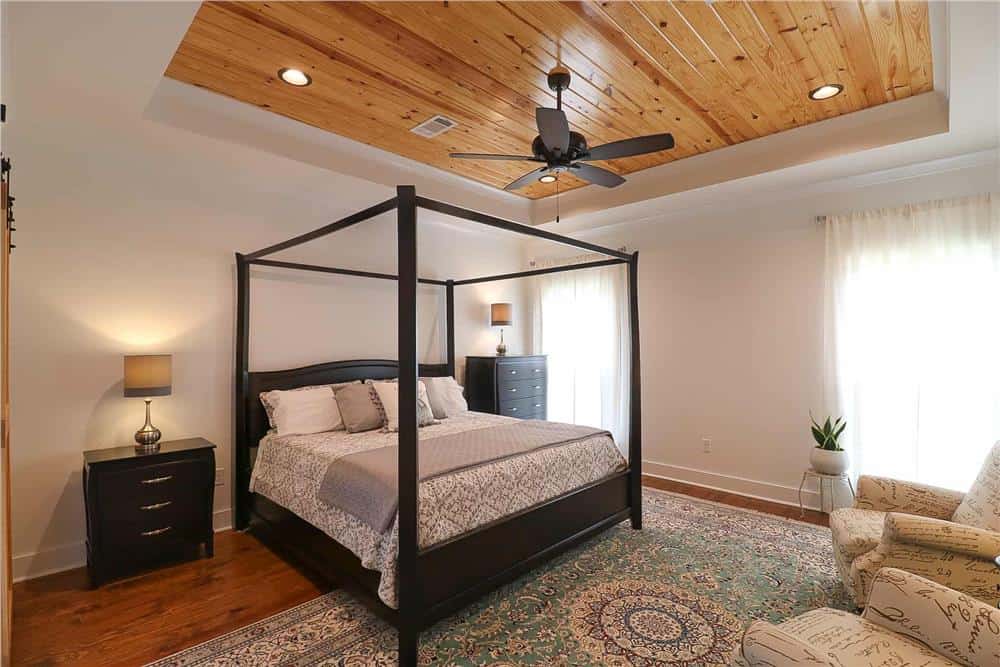 The primary bedroom features a dark wood canopy bed and a tray ceiling clad in wood planks.