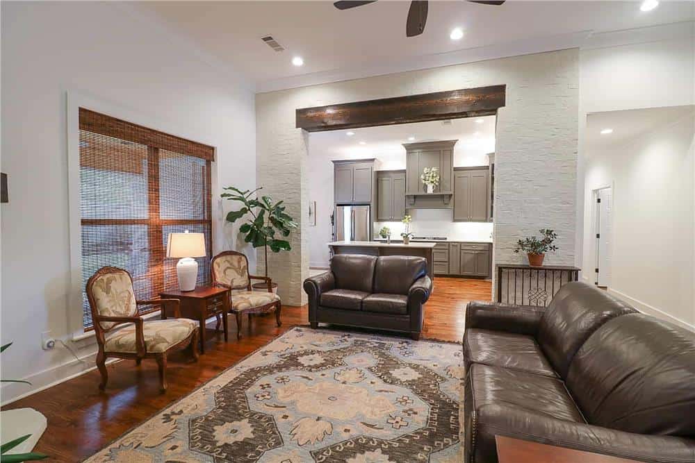 The family room has leather sofas and wooden armchairs that blend in with the warm hardwood floor.