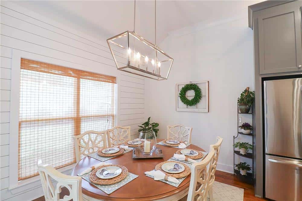 Framed windows and a linear chandelier suspended over the oval table brighten the dining area.