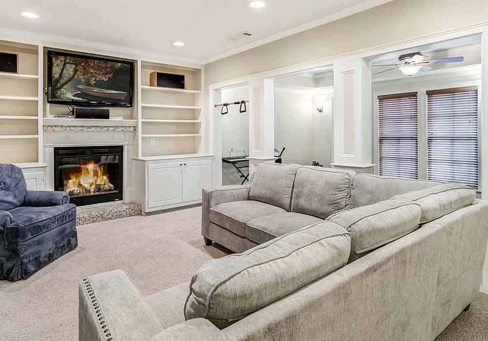 Lower-level living room with an L-shaped sectional, velvet armchair, and a fireplace flanked by built-in shelves and cabinets.