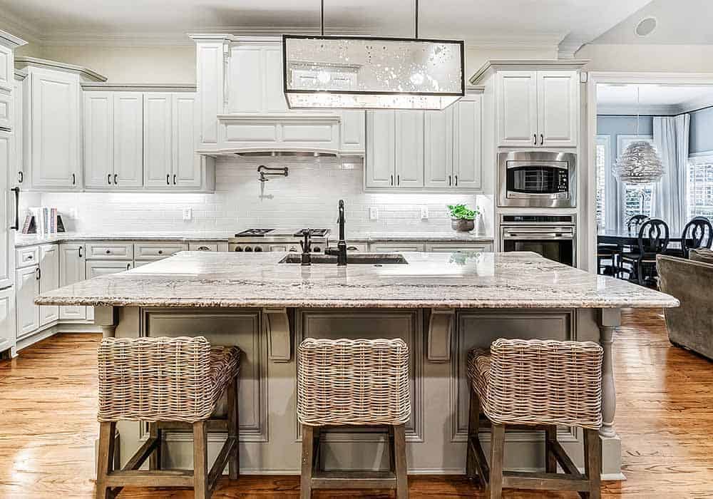 The kitchen offers premium appliances, white cabinetry, and a large island paired with wicker bar stools.