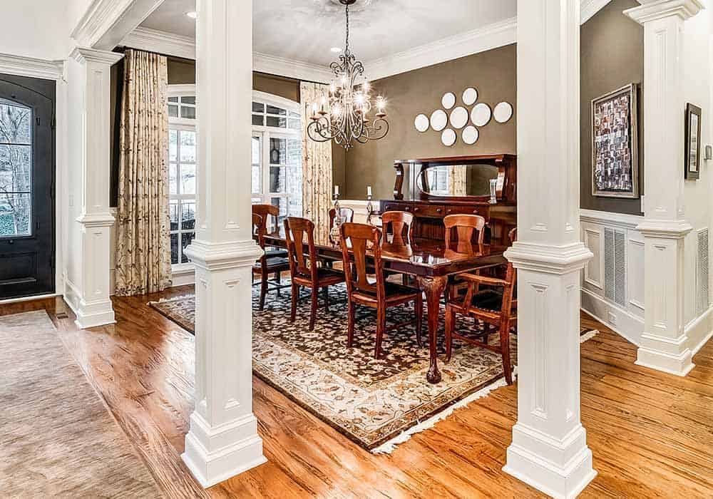 The formal dining room has an ornate chandelier and a wooden dining set sitting on a tasseled area rug.