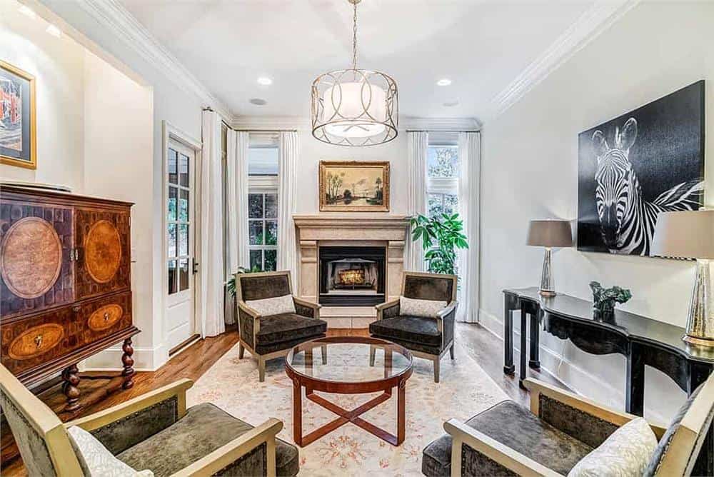 Family room with a fireplace and velvet armchairs surrounding a glass-top table.