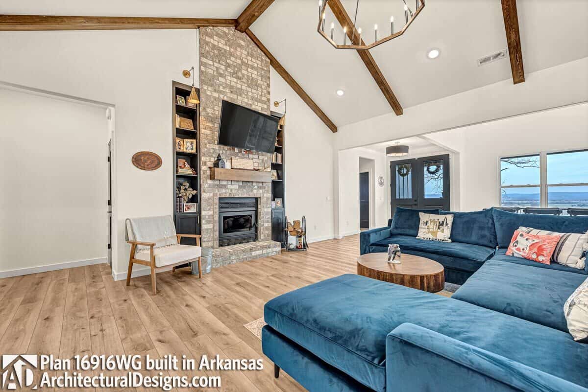 The family room includes a velvet sofa and a stone fireplace flanked by inset shelves.