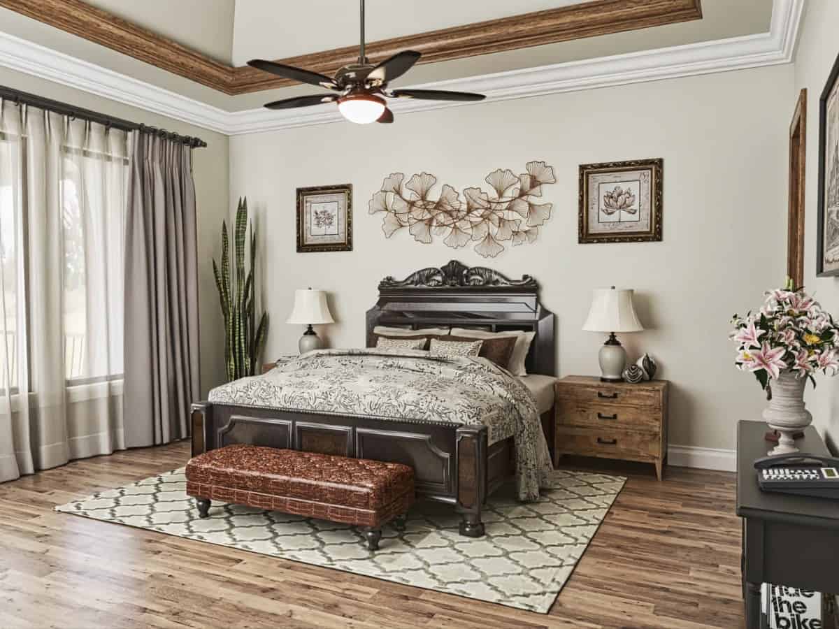 The primary bedroom has a tray ceiling and a dark wood bed complemented with a leather tufted bench.