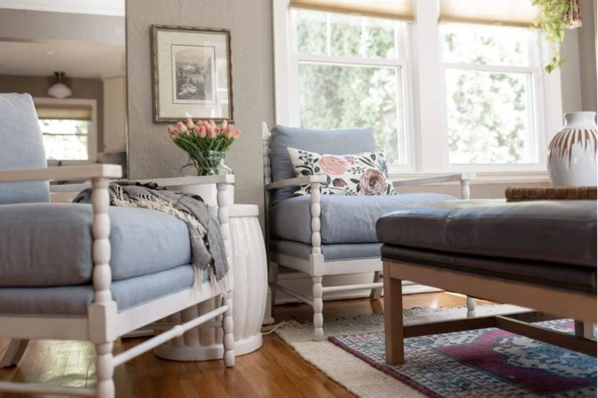 Two white chairs with floral pillows, and a flower vase.