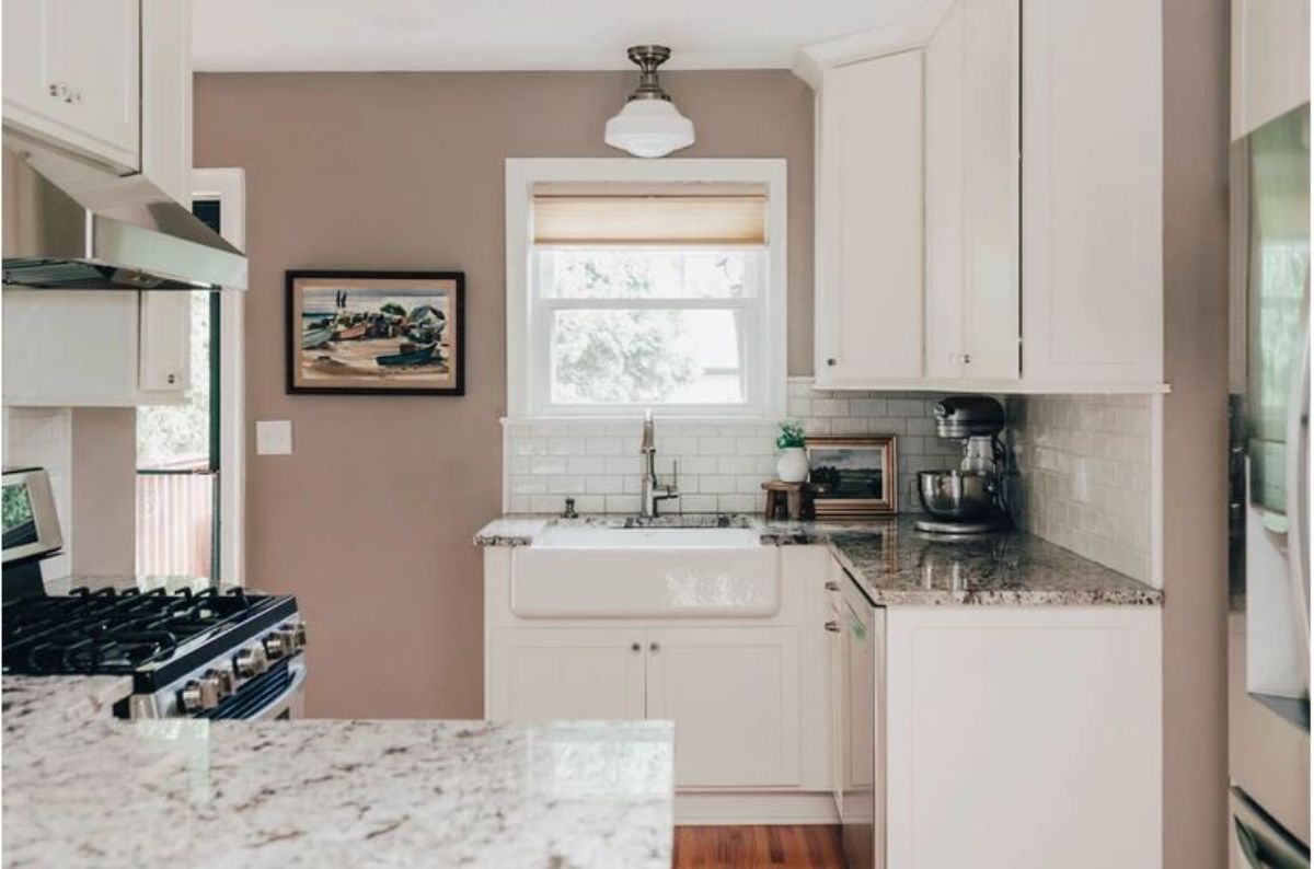 Kitchen setting with a sink facing the window, white cabinets, and a coffee maker.