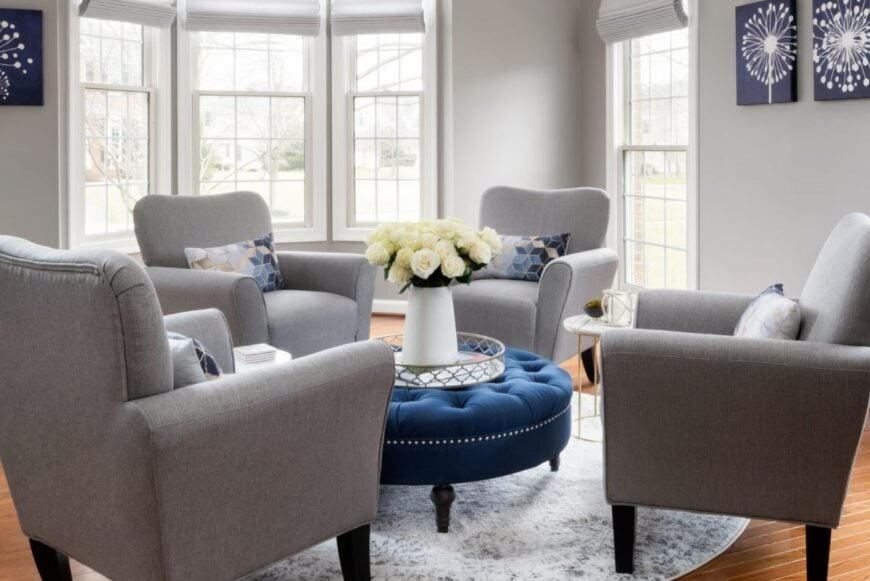 The vibrant and inviting formal living room bathed in an abundance of natural light. The room exudes an aura of comfort and elegance, with the set of four lounge chairs arranged in a spacious and symmetrical manner. The floor boasts a rich, polished wooden surface, and the walls are complemented by the beautiful artwork of abstract modern dandelions. 