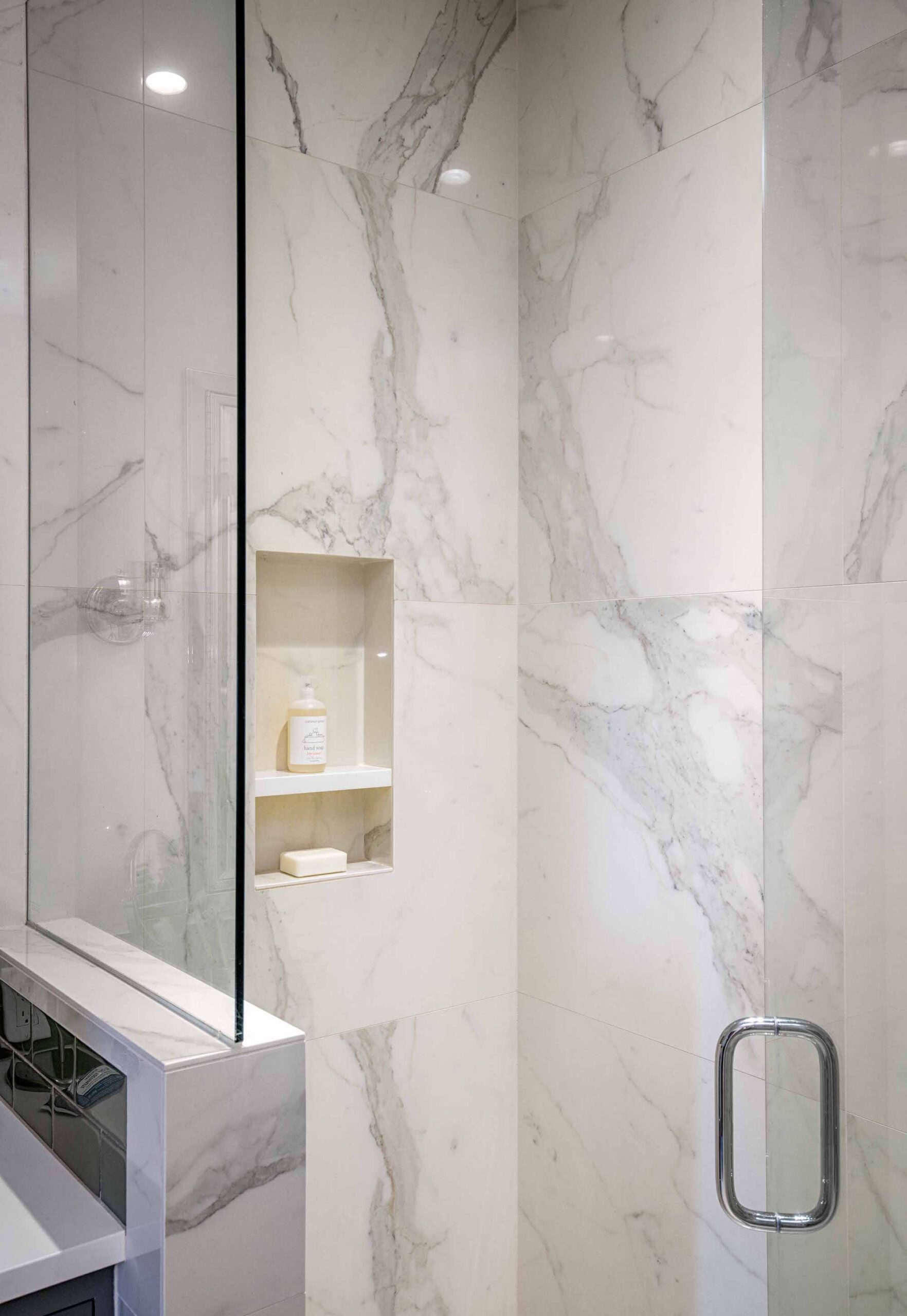The shower with a beautiful white tiles and a transparent door.