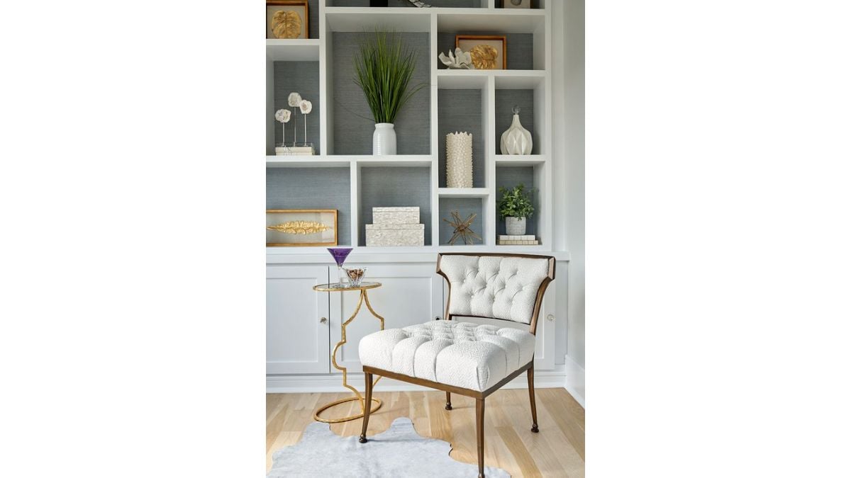 A cabinet was behind the lovely white chair with gold trim.