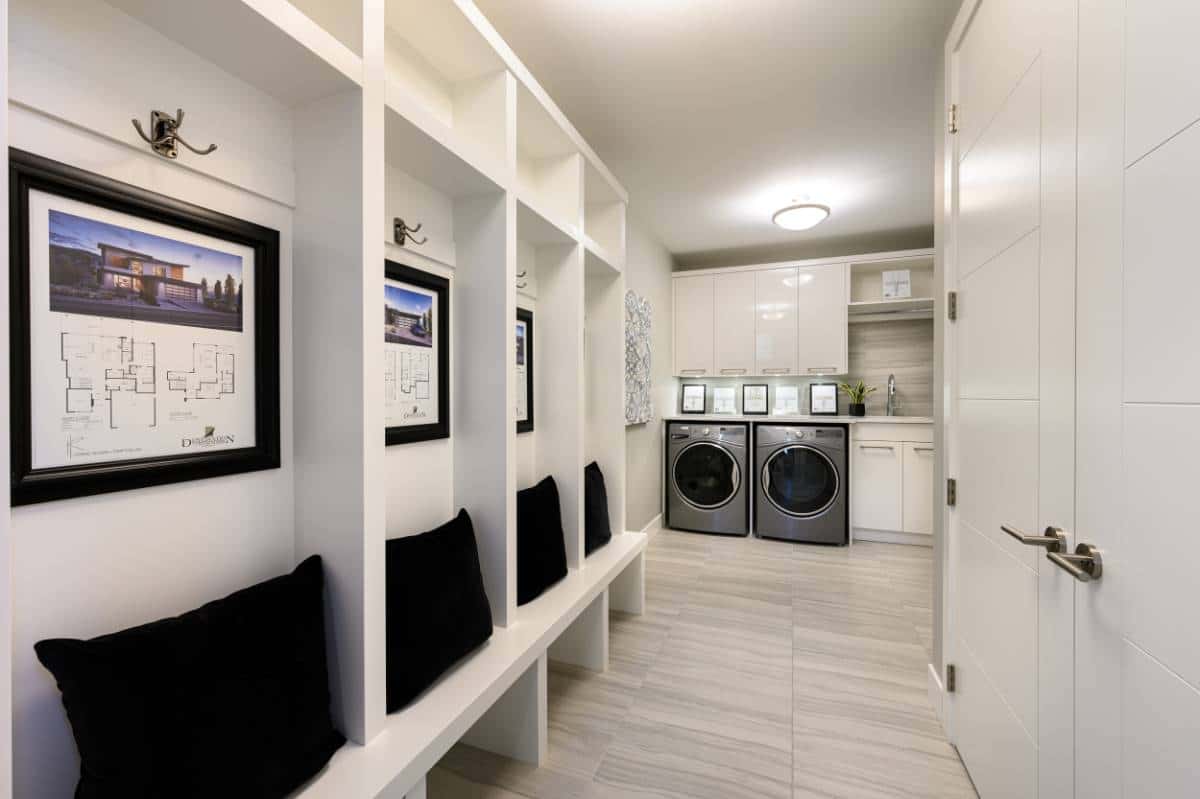 Combined laundry and mudroom with built-in seats, storage shelves, front-load appliances, and overhead cabinets.