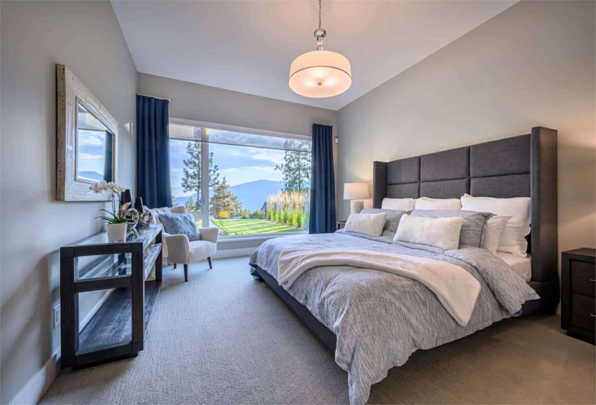Primary bedroom with a wingback upholstered bed and large windows overlooking the backyard.