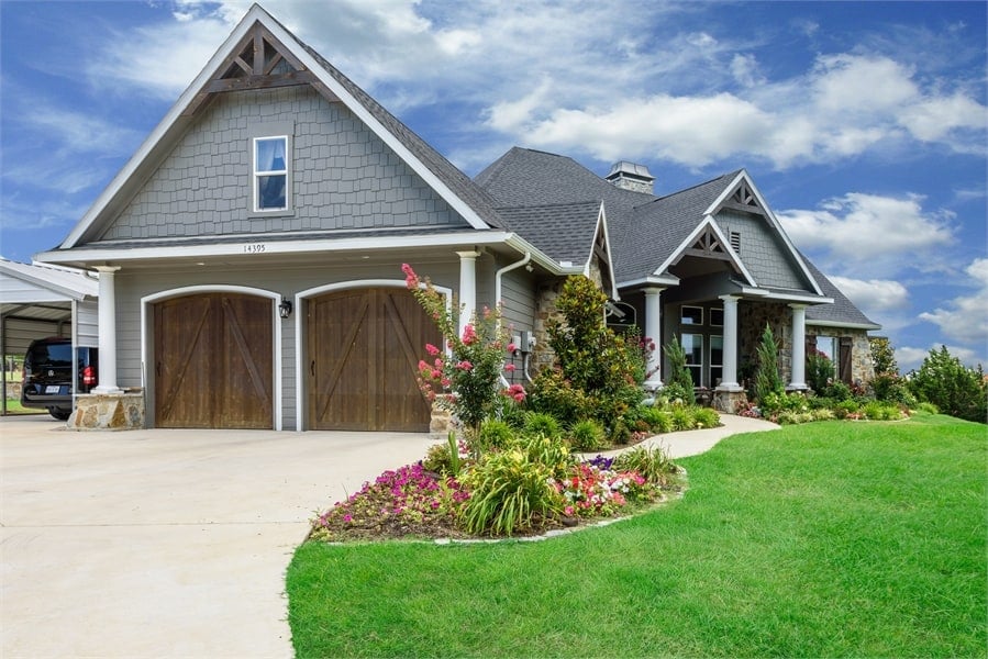 Front-left exterior view showcasing the angled 2-car garage enclosed in arched wooden doors.