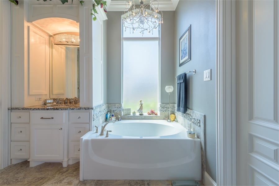 A tall picture window and beaded chandelier illuminate the bathtub.