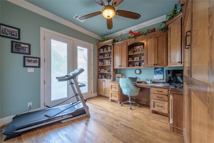 The home office has outdoor access and wooden built-ins that blend in with the hardwood floor.