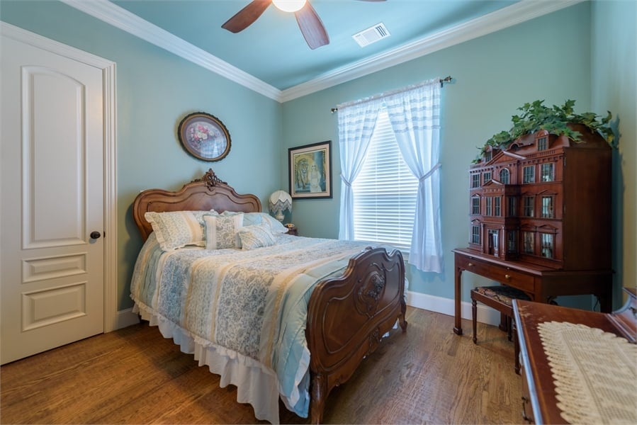 This bedroom has wooden furnishings and light blue walls adorned with framed artworks.