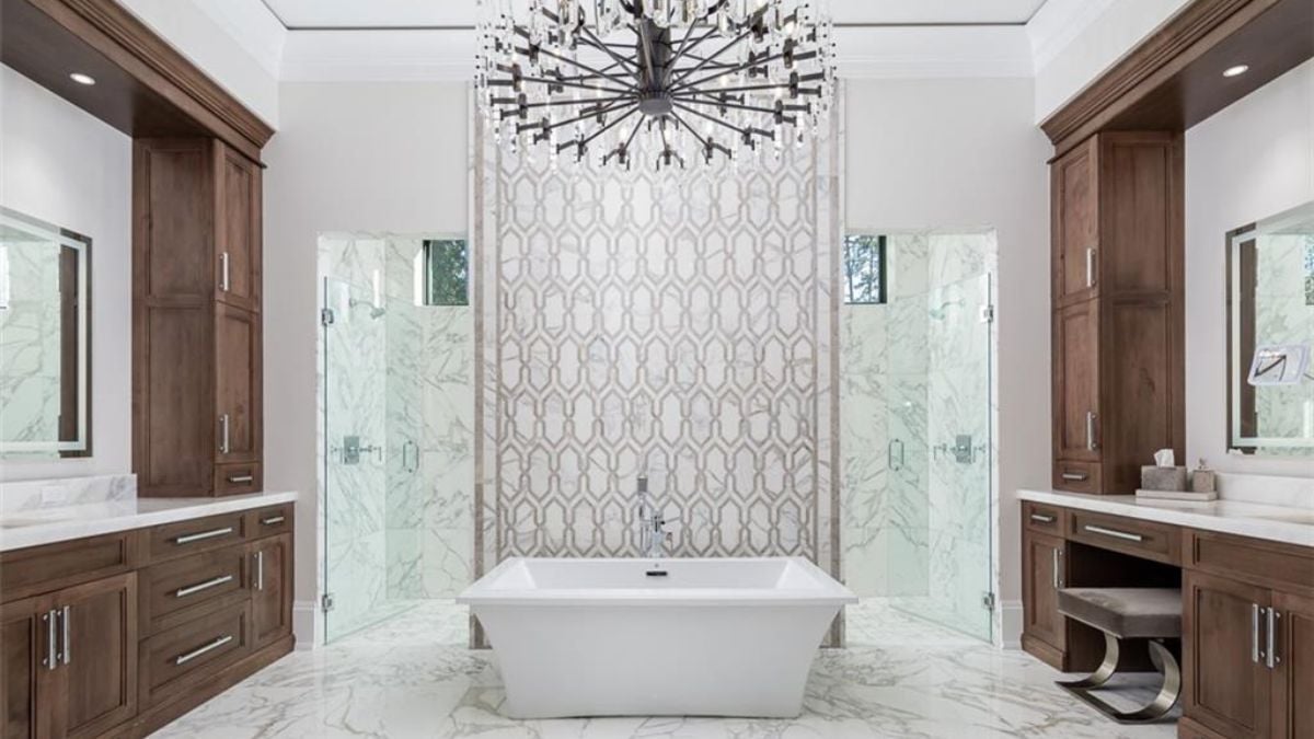 A stunning bathroom with tub, chandelier and wooden designed dresser.