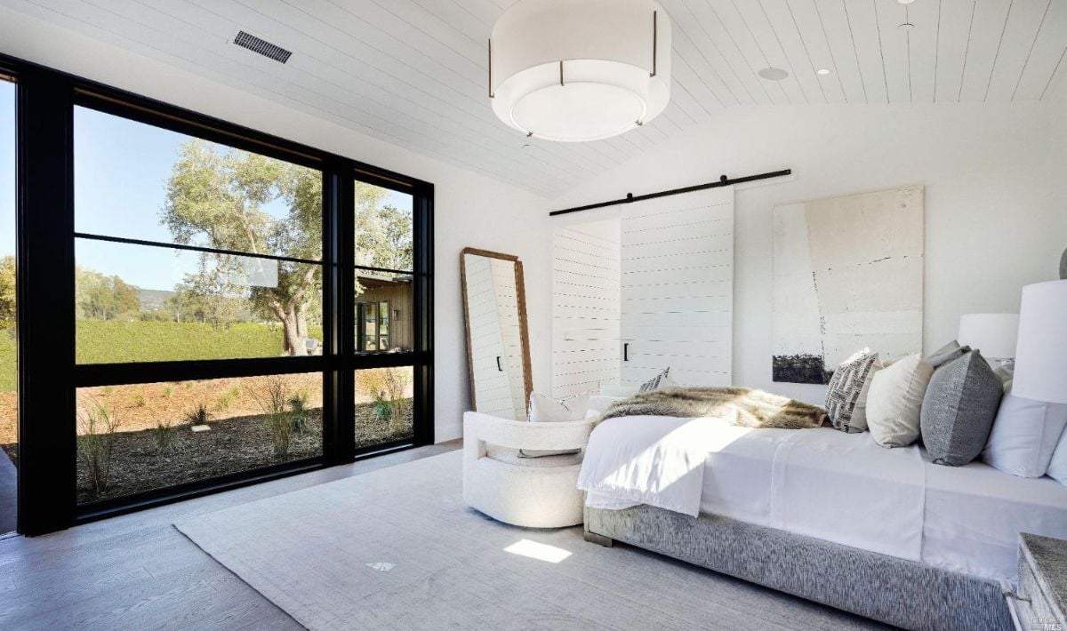 Bedroom with a huge sliding glass doors, a large bed and wood flooring.