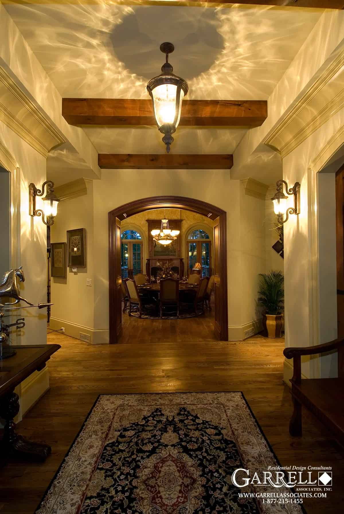 Foyer with a beamed ceiling and a vintage rug that lays on the hardwood flooring.