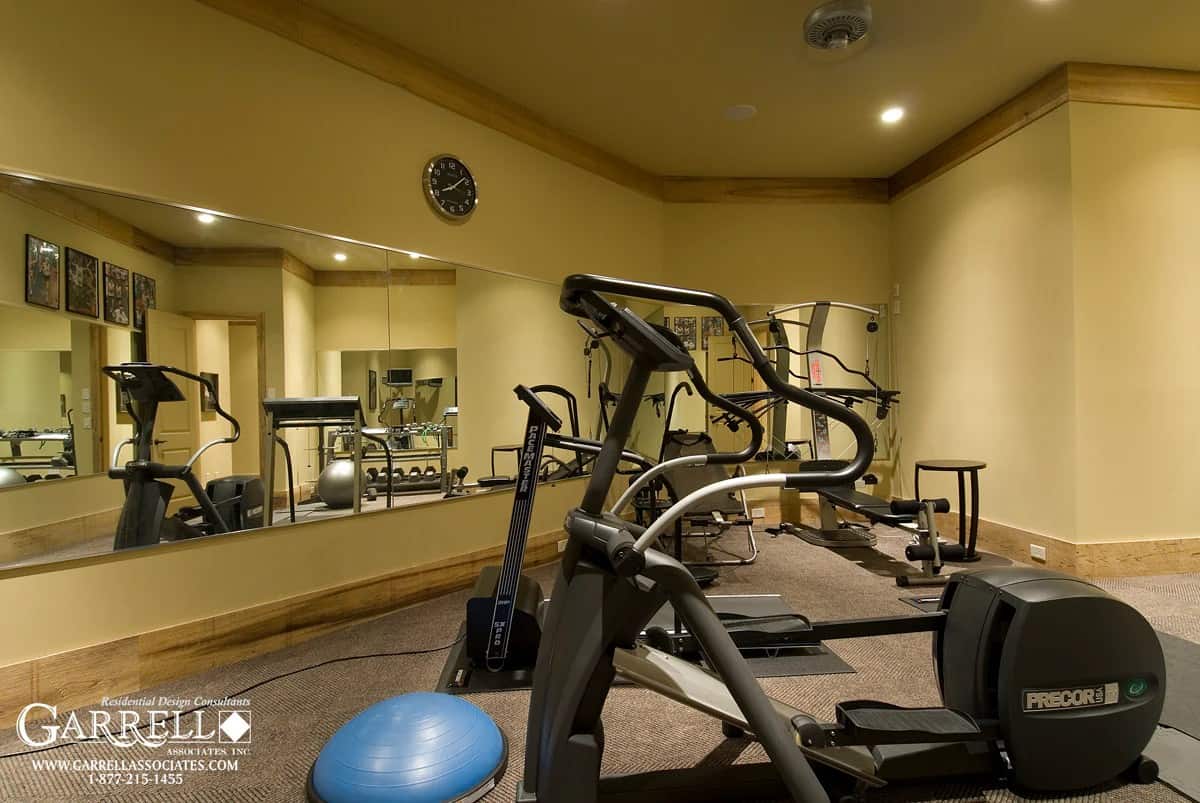 Home gym with expansive mirror, carpeted floor, and beige walls lined with wooden moldings.
