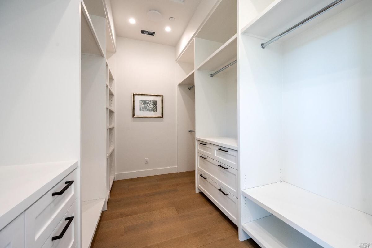 Walk-in closet with white cabinets and drawers.