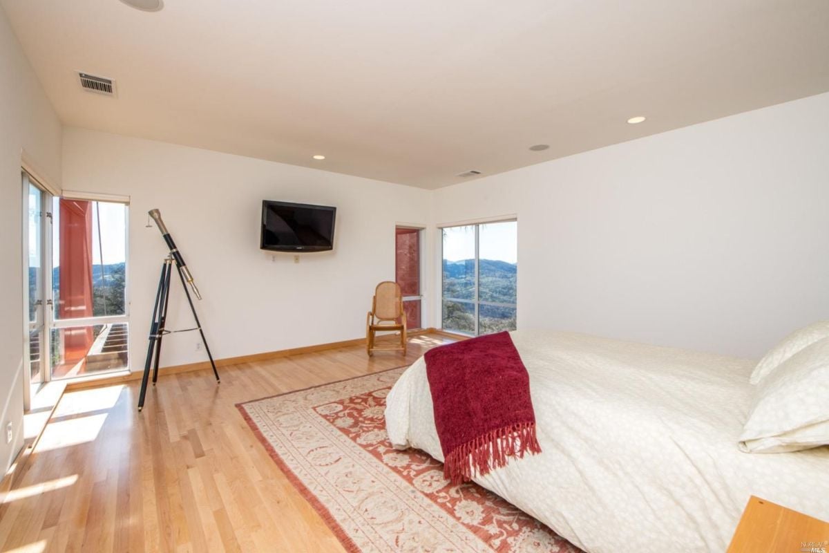 Bedroom with wood floors, television and glass windows.