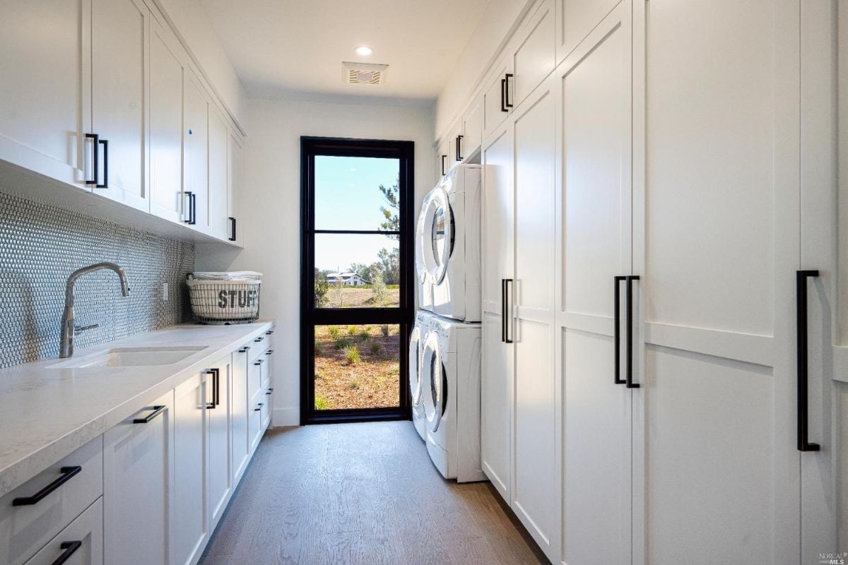 Laundry room with a sink, white cabinets and a washer.