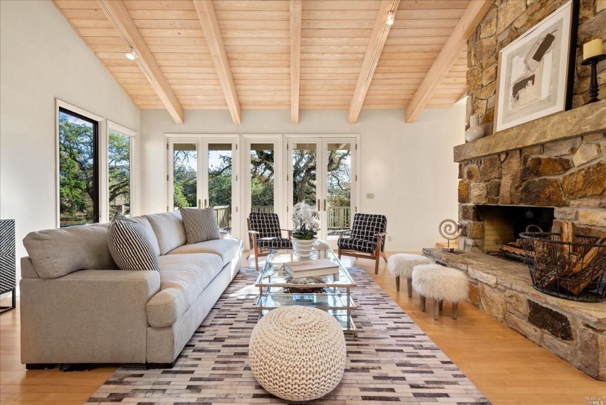 Living room with a stone fireplace and large glass windows.