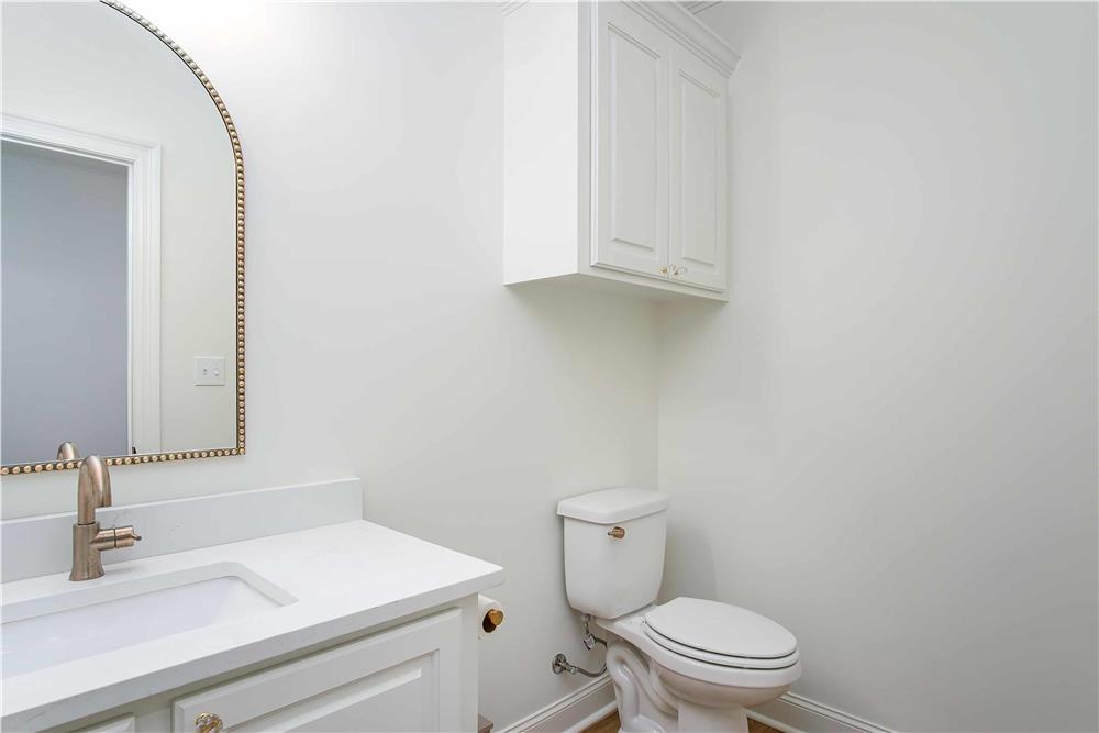 Powder room with an overhead cabinet, a toilet, and a sink vanity adorned with an arched mirror.