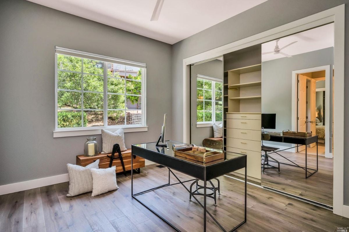 Home office with a desk, wood flooring and glass windows.