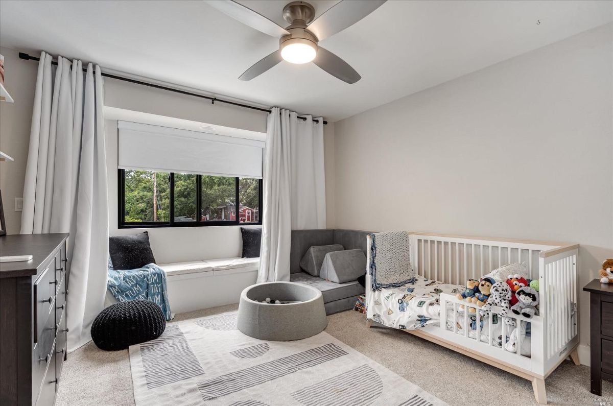 Carpeted kid's room with ceiling fan and glass windows.